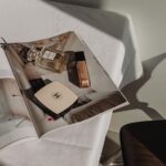 Ein offenes Magazin liegt im warmen Sonnenlicht, darauf stehen ein Chanel-No.-5-Flakon und ein Dior-Concealer.