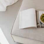 Auf einem beigen Polstersofa liegt ein aufgeschlagenes Magazin neben einer Schale mit grünen Trauben im weichen Tageslicht.