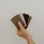 Eine Hand hält mehrere Farb- und Materialmuster in Braun-, Grau- und Weißtönen vor hellem Hintergrund.