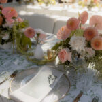 Ein festlich gedeckter Hochzeitstisch zeigt roséfarbene Blumenarrangements, feines Glasgeschirr und natürliches Tageslicht.