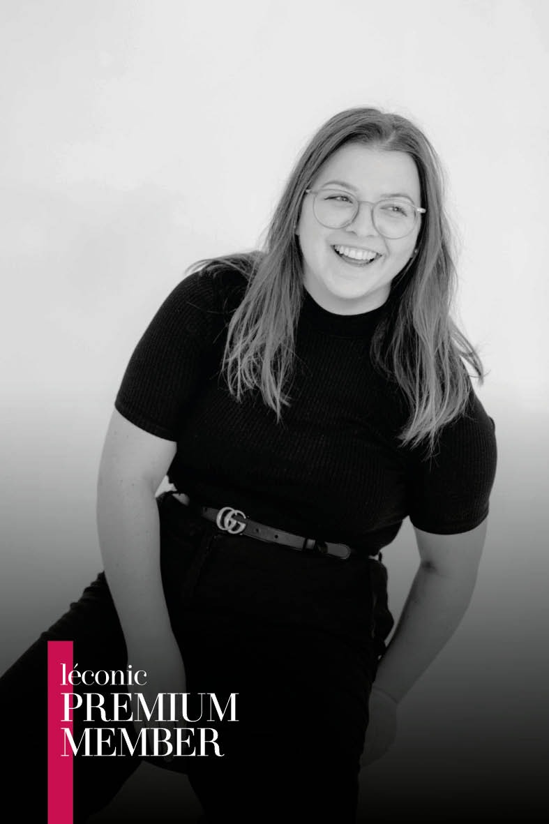Diana Fischer lacht in schwarzer Kleidung und mit Brille vor einem hellen, reduzierten Hintergrund.