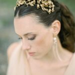 Eine Frau mit dunklem, zurückgebundenem Haar trägt einen goldfarbenen Haarreif und lange Ohrringe vor grünem Hintergrund.