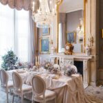 Ein festlich gedeckter Tisch steht in einem prunkvollen Salon mit Kronleuchter, Goldornamenten und zarten Pastellblumen.