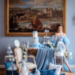 Vor einem großen Historiengemälde steht ein opulentes Dessert-Arrangement in Blautönen mit einer Frau im hellblauen Kleid.