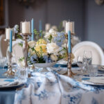 Ein festlich gedeckter Tisch mit weiß-blauer Floristik, silbernen Kerzenständern und feinem Porzellan in ruhiger Atmosphäre.