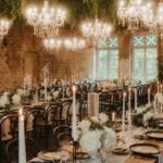 Ein festlich gedeckter Saal mit Kronleuchtern, Kerzen und weißen Blumenarrangements wirkt warm und elegant.